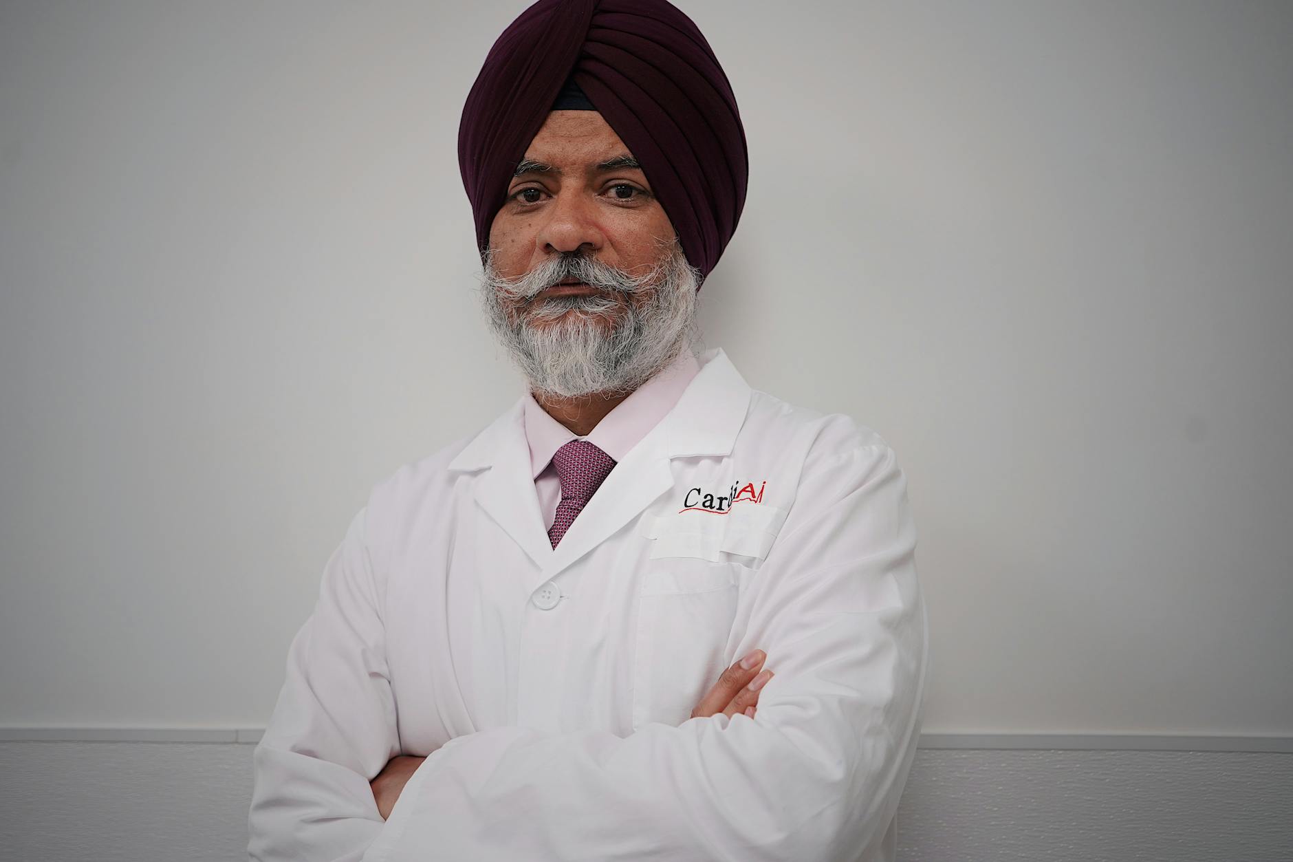 Portrait of a confident doctor standing with arms crossed, wearing a white coat and turban.