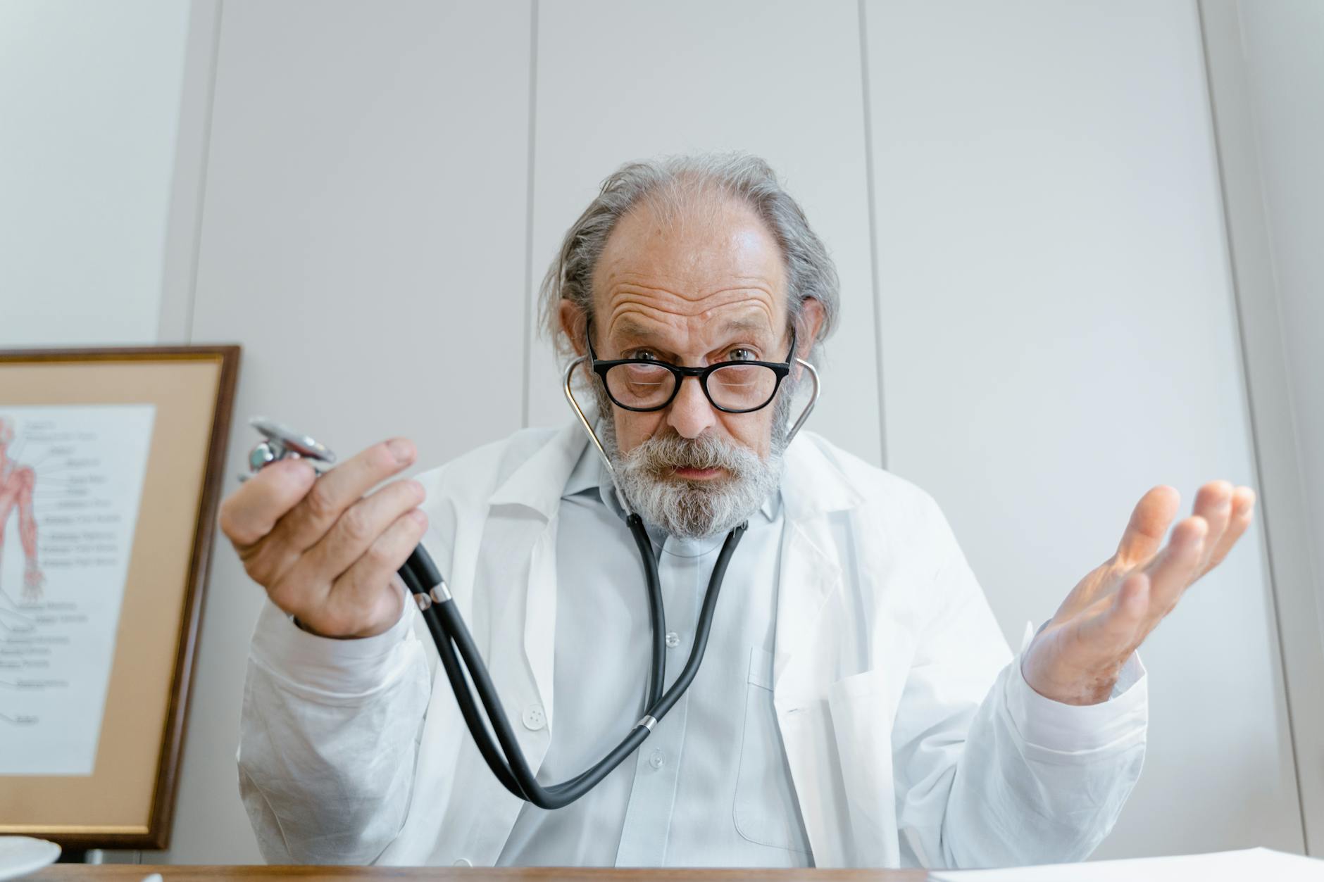 Senior doctor gesturing with stethoscope in a clinical setting, emphasizing telemedicine.
