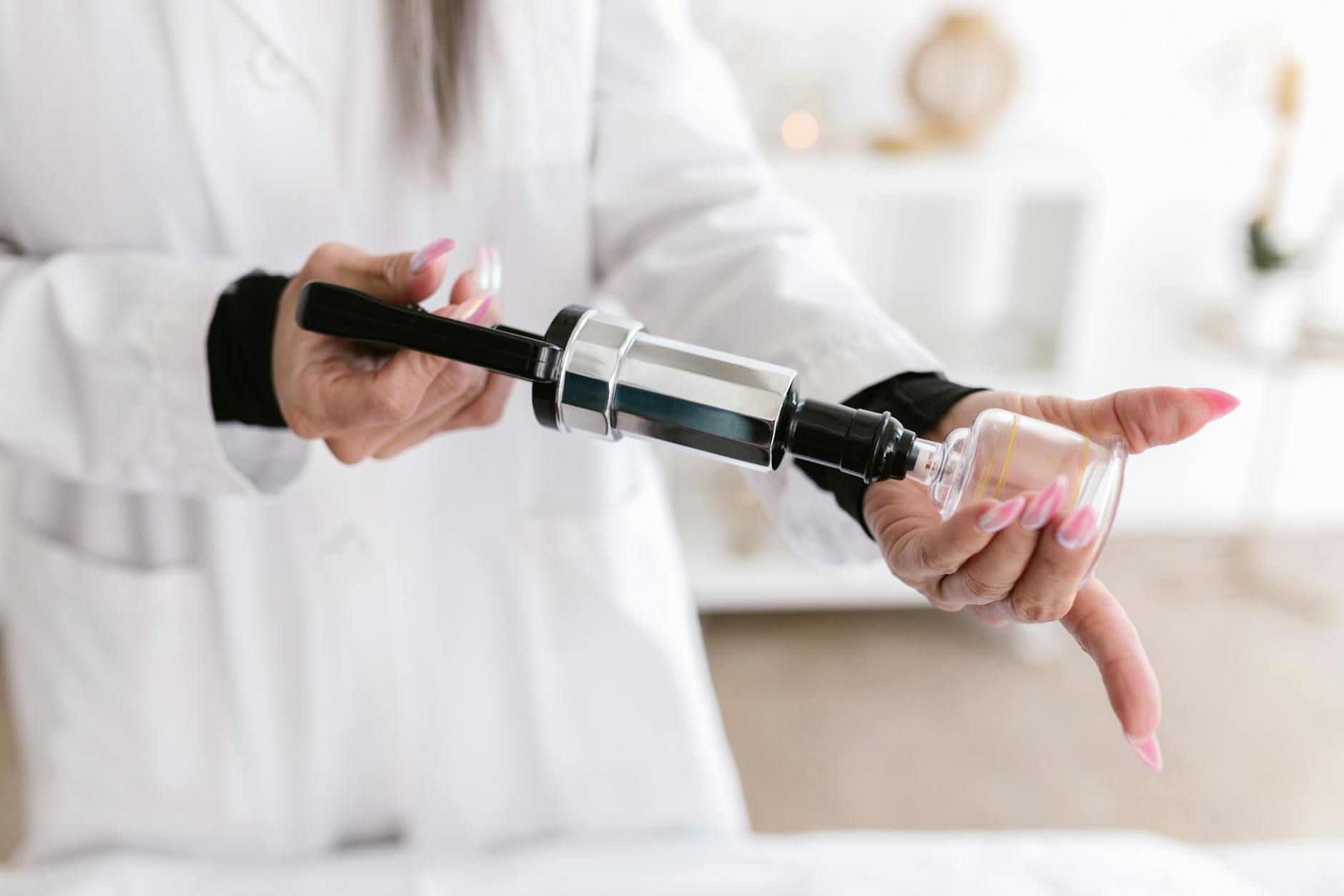 A woman in a lab coat holding a cupping therapy device, focusing on hands and tool.