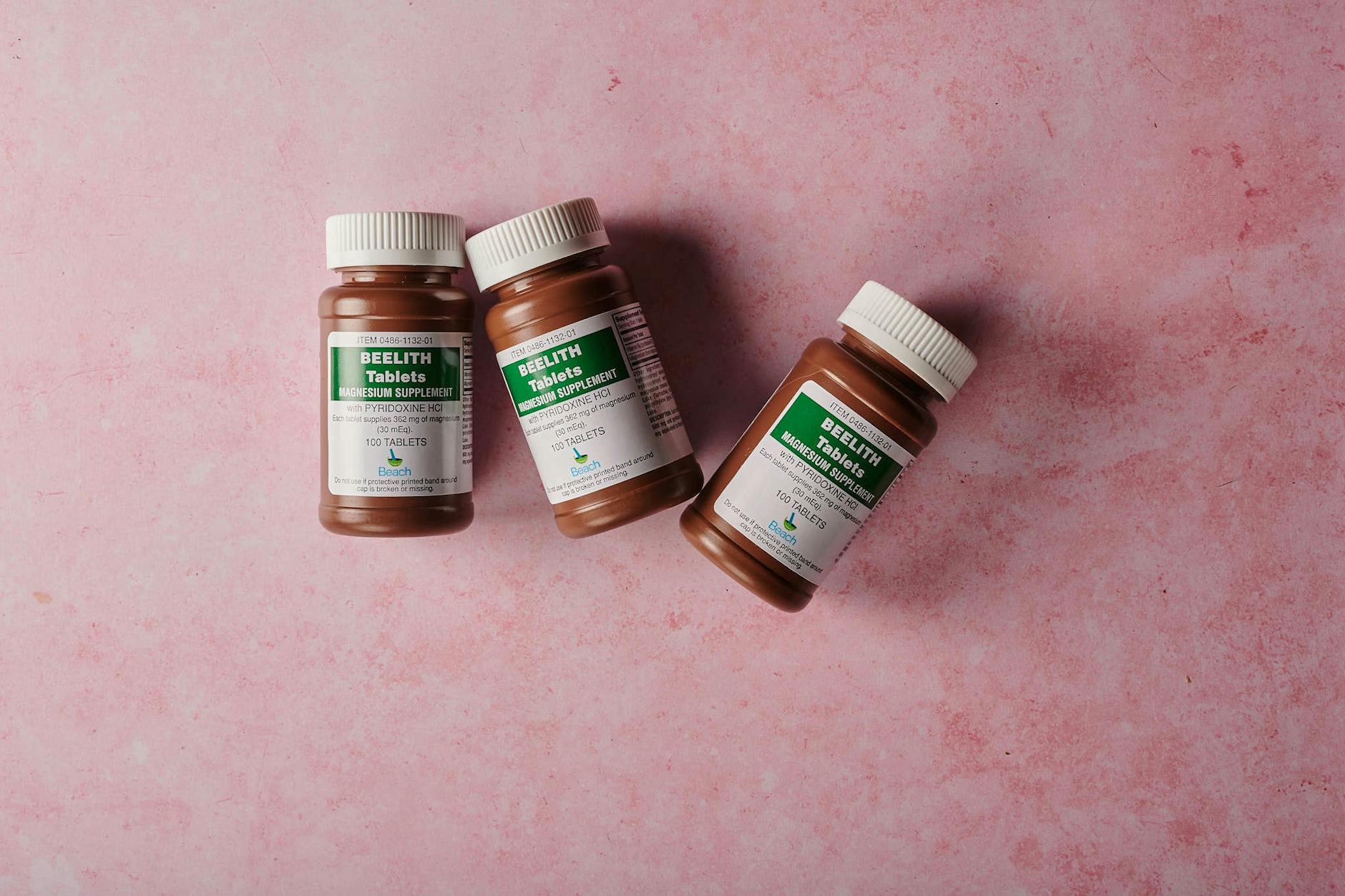 Three brown bottles of magnesium tablets on a soft pink background, ideal for health-themed content.