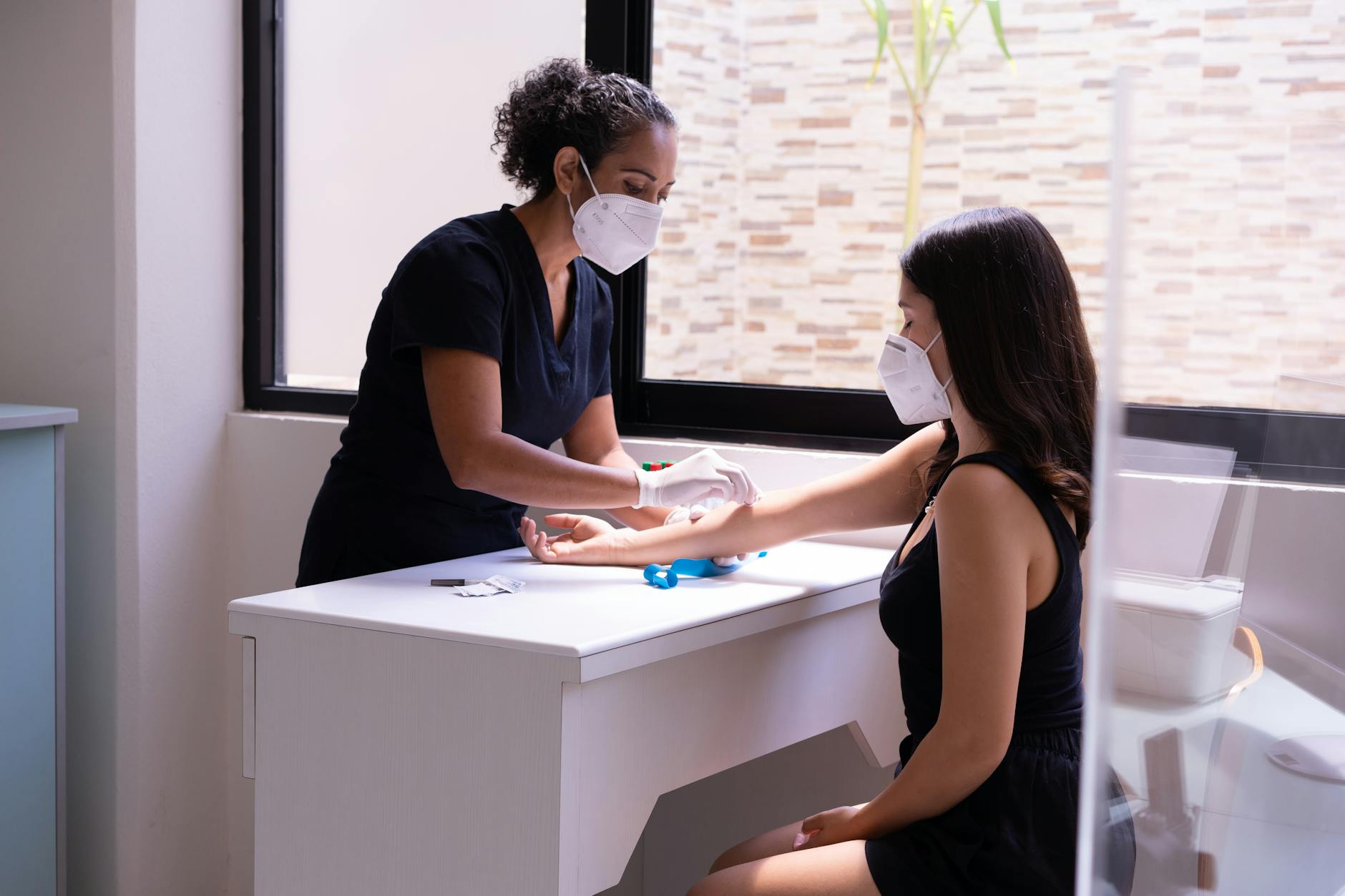 A healthcare professional wearing a face mask performs a blood test on a female patient in a clinic.