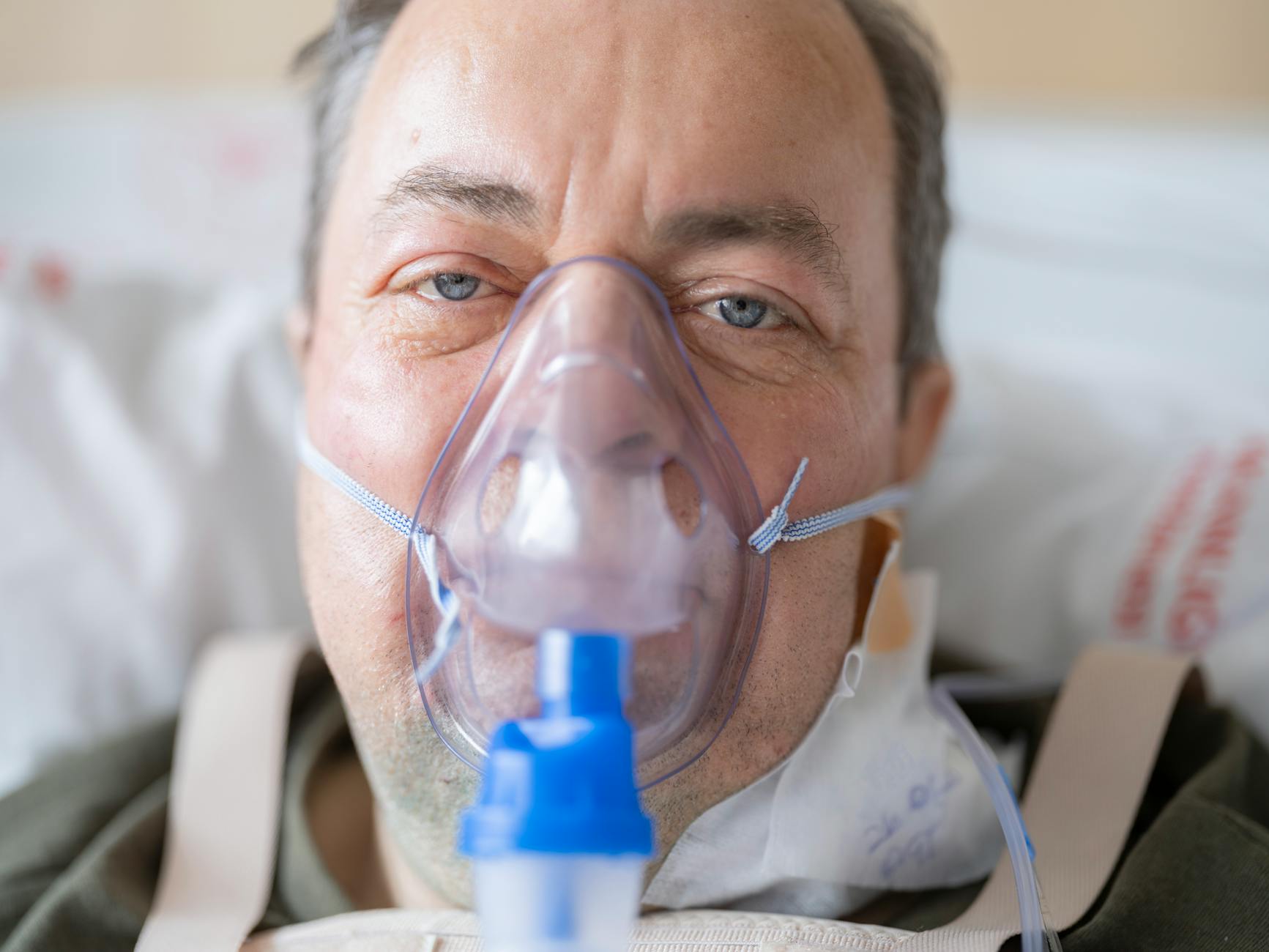 Close-up of a man in a hospital bed wearing an oxygen mask, highlighting healthcare needs.