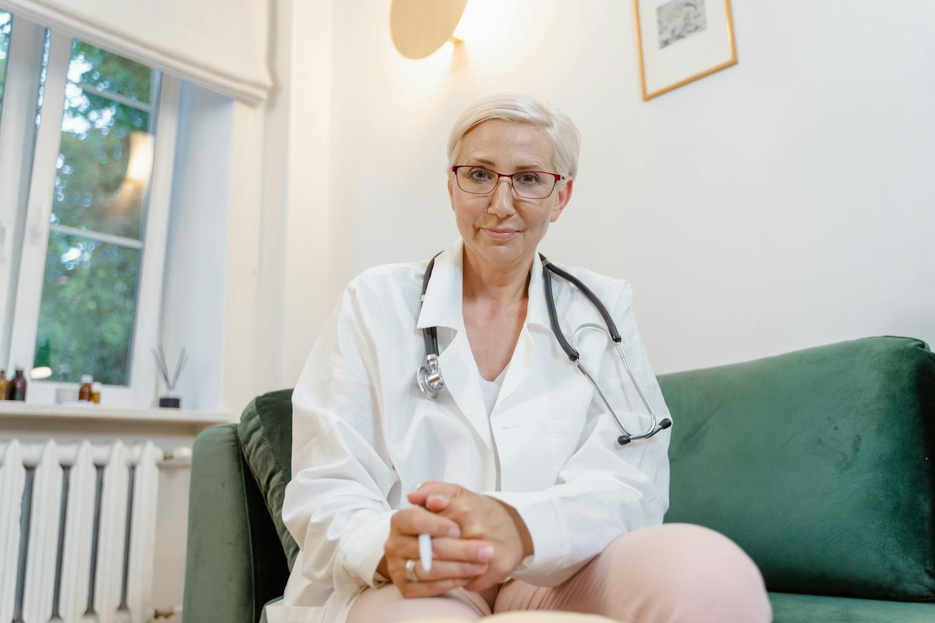 Caucasian female doctor with eyeglasses and stethoscope in a modern clinic setting.