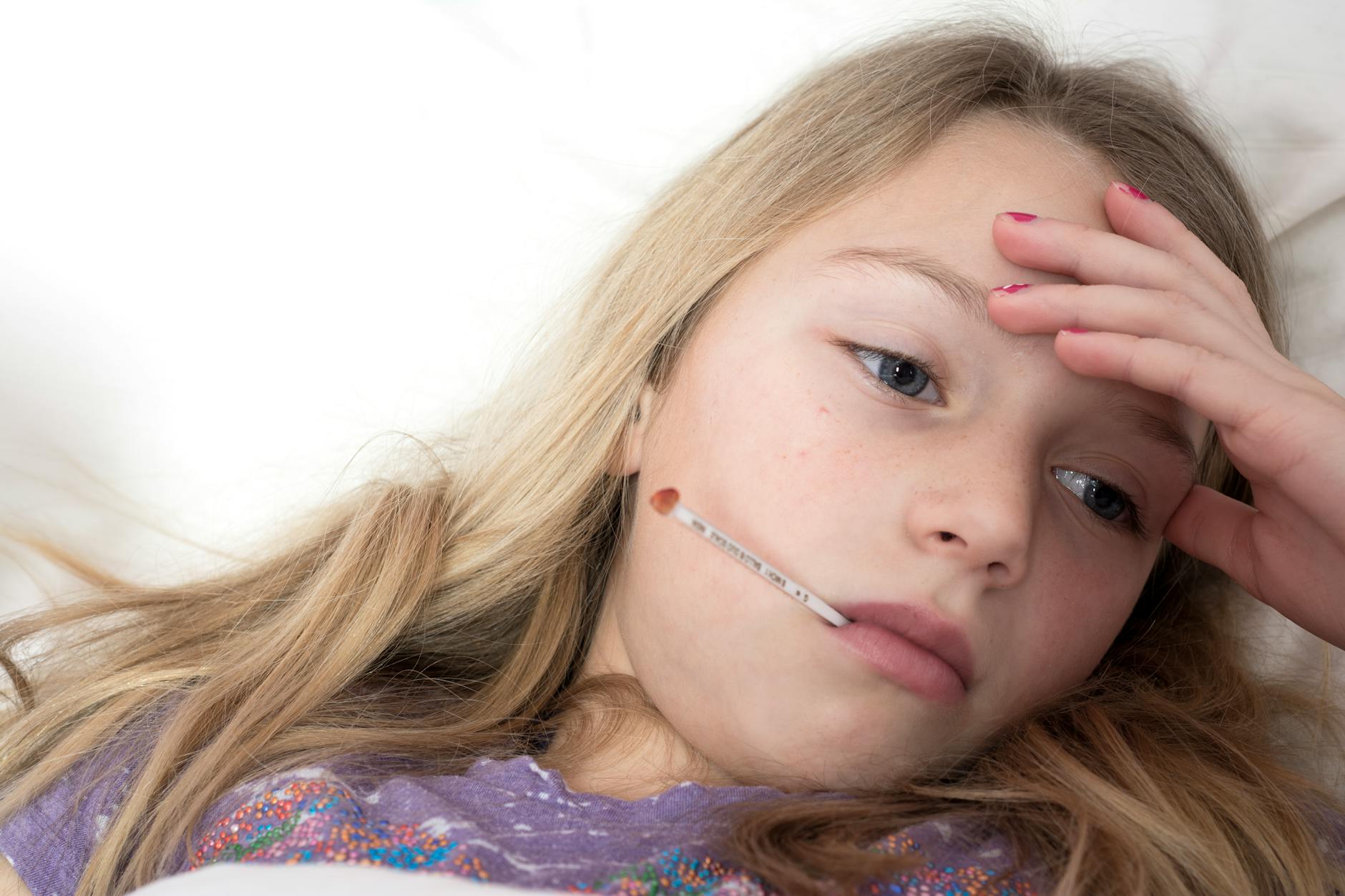 A young girl rests in bed with a thermometer, illustrating signs of illness and fatigue.