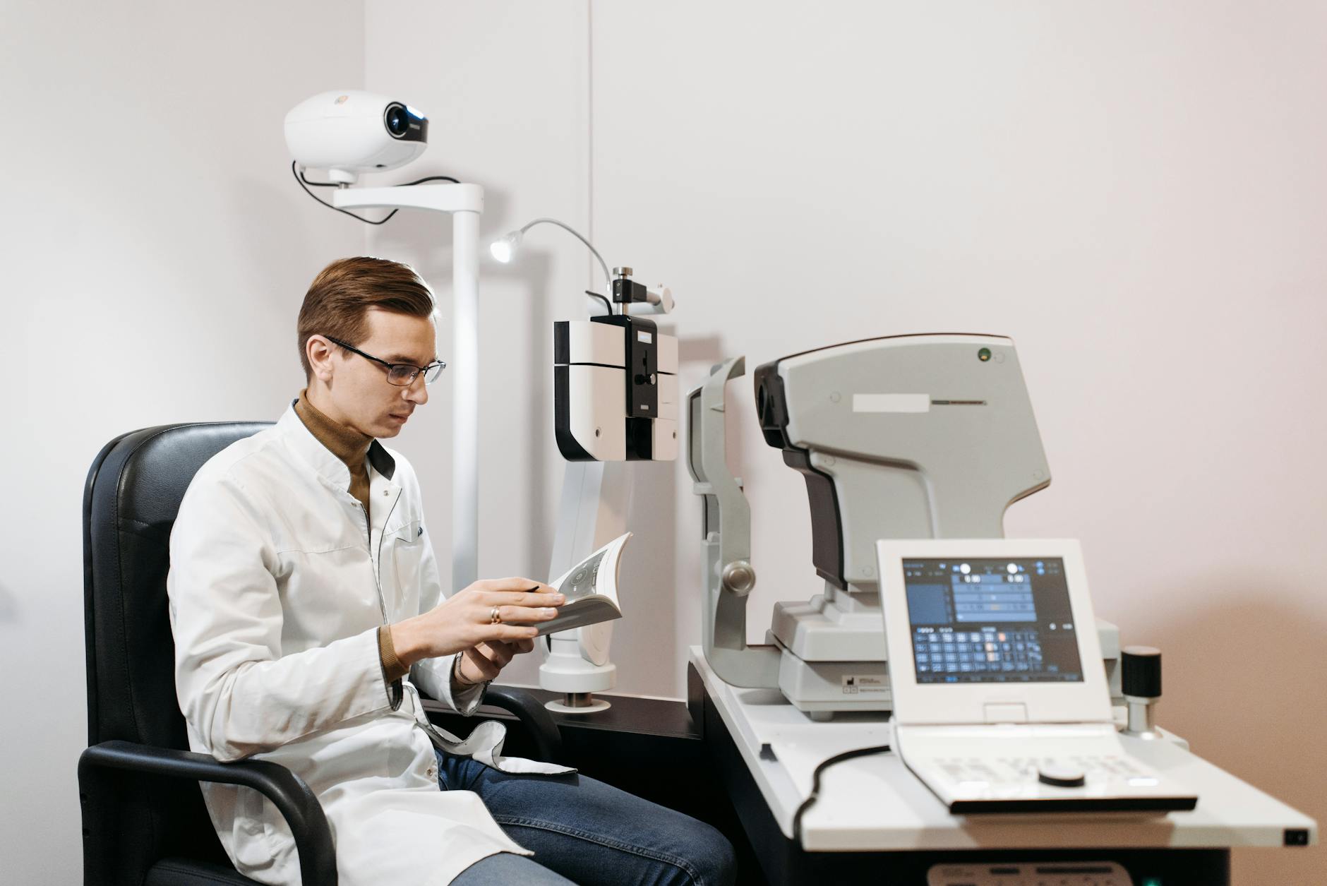 Eye care professional in clinic using ophthalmology equipment, wearing glasses and a lab coat.