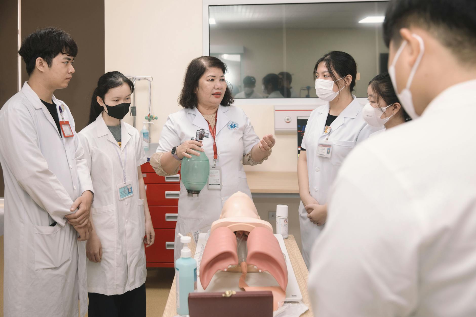 Group of medical students practicing skills with a training mannequin in a classroom setting.