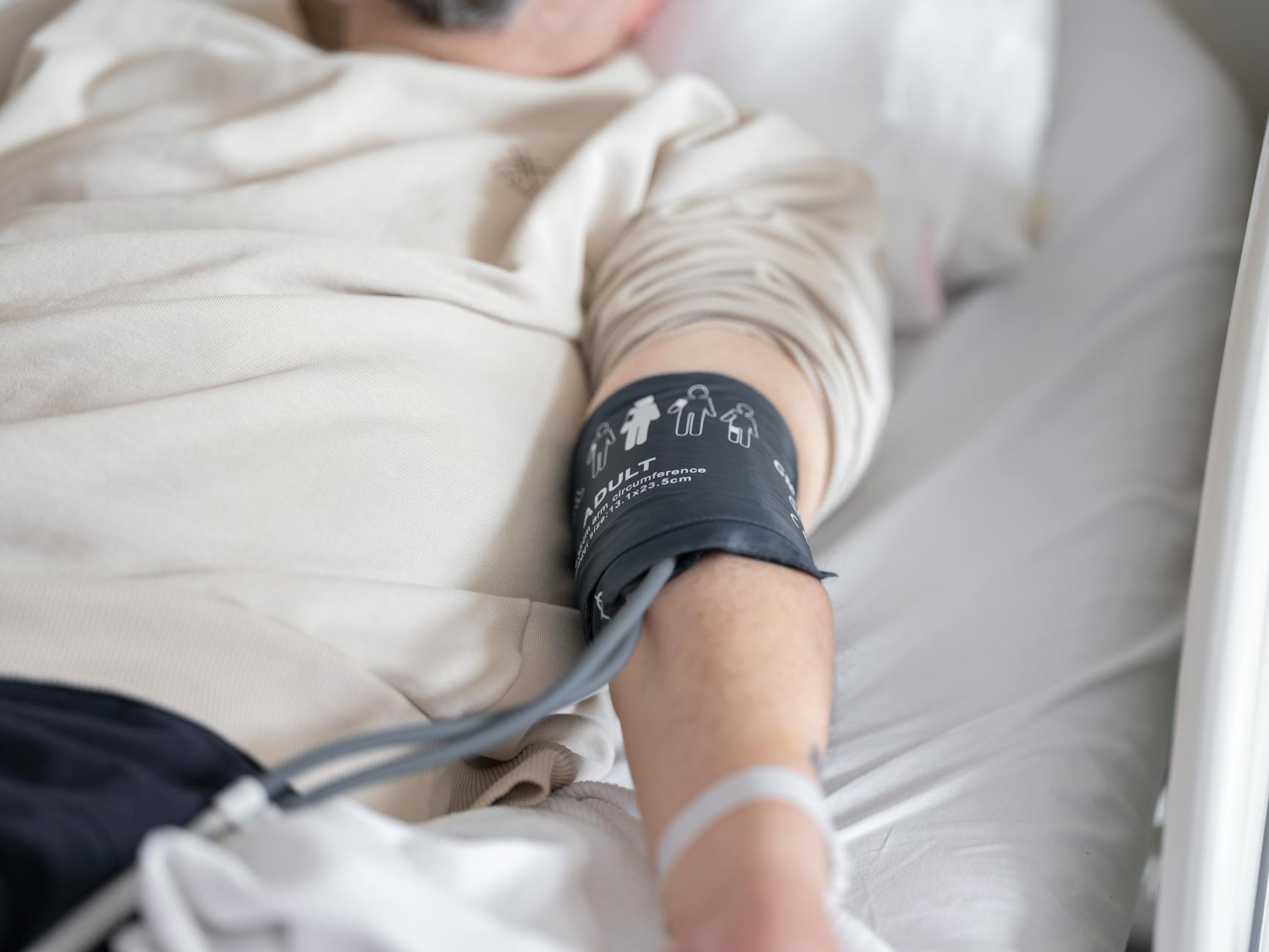Close-up of patient in hospital bed with blood pressure cuff on arm, emphasizing healthcare theme.