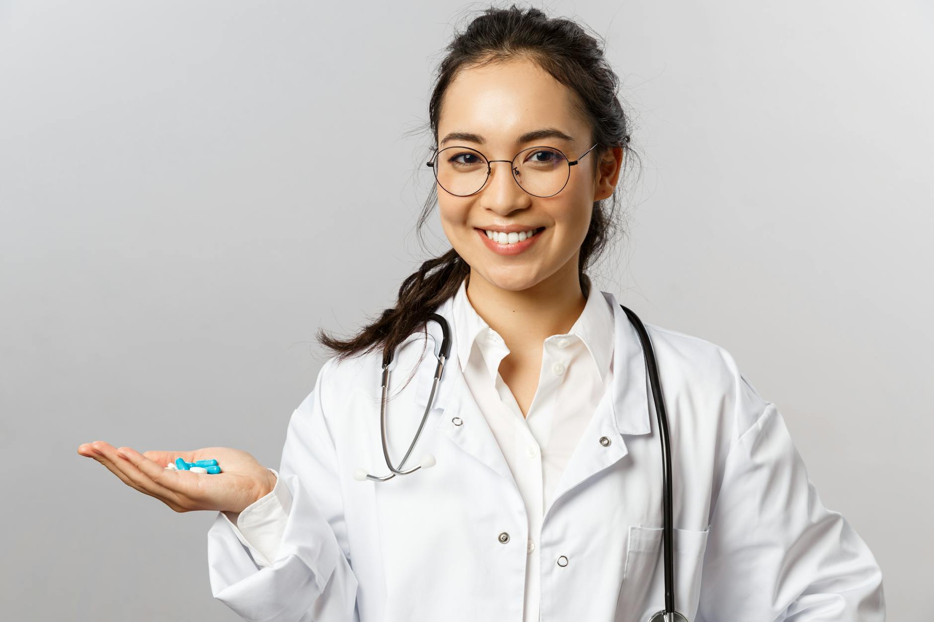 Asian female doctor smiling while holding pills. Promoting healthcare and medicine.